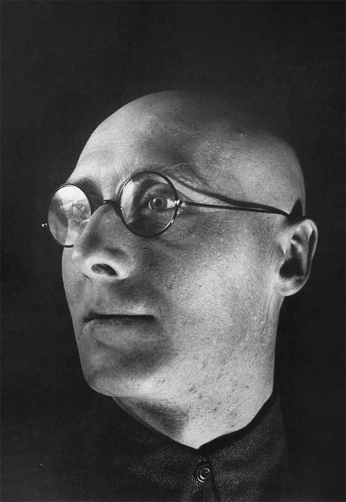 Black and white photograph of Alexander Rodchenko taken at an unknown date. Picture shows a bald man in glasses looking towards left. 