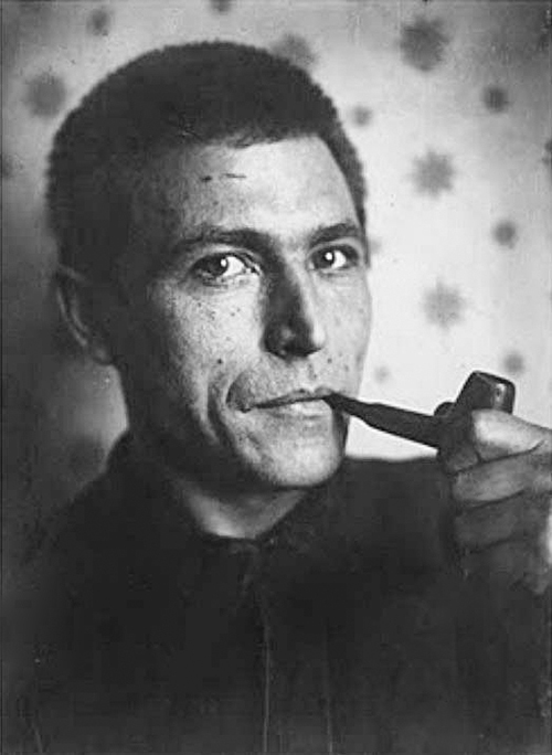 Black and white photograph of Gustav Klutsis taken at an unknown date. Picture depicts a shorthaired man smoking a pipe